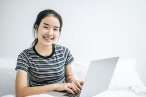 una giovane donna che gioca sul suo portatile a letto foto