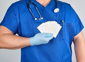 medico nel sterile latice guanti e blu uniforme detiene un' vuoto bianca attività commerciale carta foto