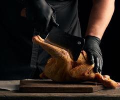 capocuoco nel nero uniforme e latice guanti chopping crudo pollo in pezzi foto