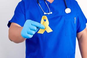 medico nel un' blu uniforme e sterile latice guanti detiene un' giallo nastro nel il suo mano foto