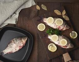fresco carassio pesce cosparso con spezie e Limone fette e bugie su un' Marrone di legno taglio tavola foto
