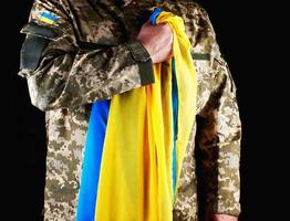 ucraino soldato detiene nel il suo mano il giallo-blu bandiera di il stato, lui premuto il suo mano per il suo il petto foto