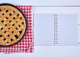 il giro nero ribes torta e un Aperto taccuino con vuoto bianca lenzuola foto