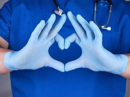 medico nel blu uniforme e vecchio latice guanti mostrando cuore gesto foto