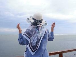 indietro di il donna nel il cappello su il tropicale spiaggia chi era guardare su a il cielo e il mare mentre sua mani formato amore a partire dal il ponte. spiaggia Visualizza foto