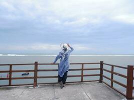 indietro di il donna nel il cappello su il tropicale spiaggia chi era guardare a il cielo e il mare mentre diffusione sua mani su il ponte. mare Visualizza foto