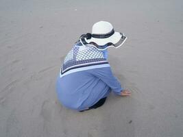 indietro di il donna nel il cappello chi era seduta e giocando spiaggia sabbia, il Visualizza di il sabbia foto