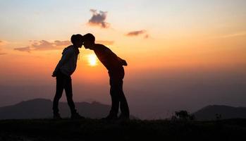 silhouette di un' coppia su il montagna, un' giovane romantico coppia godere un' bellissimo Visualizza di il sole ambientazione al di sopra di il montagne, amore, San Valentino giorno. foto