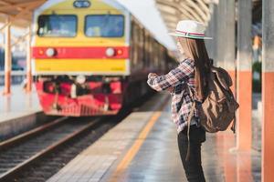 bellissimo giovane asiatico donna viaggiatore guardare orologio con Marrone Borsa ,in attesa per treno a treno stazione, Cinese turisti, viaggio e vacanza concetto. foto