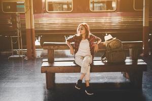 donna turistica giovane hipster con zaino seduto nella stazione ferroviaria