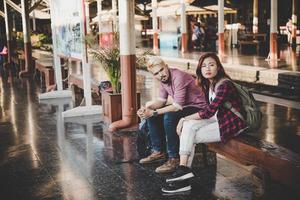 coppia giovane hipster seduto sulla panca in legno alla stazione ferroviaria foto