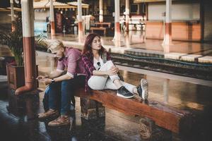 coppia giovane hipster seduto sulla panca in legno alla stazione ferroviaria foto