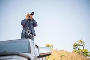 giovane fotografo seduto sul suo camioncino che fotografa una montagna