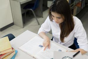 giovane studente asiatico che legge in biblioteca foto