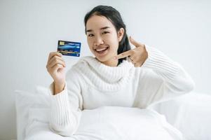 giovane donna con una carta di credito sorridente sul letto foto