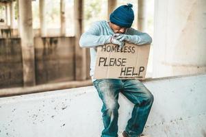 mendicante si siede su una barriera stradale con senzatetto si prega di aiutare a firmare foto