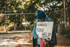 mendicante sta sulla strada con per favore aiuto segno foto