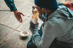 mendicante seduto sotto un ponte con una tazza di soldi e tagliatelle foto