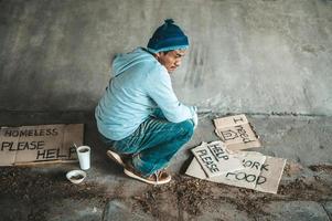 mendicante seduto sotto un ponte con cartelli di cartone per chiedere aiuto foto