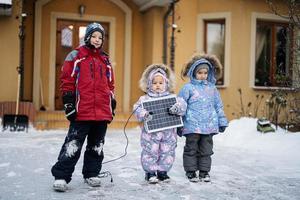 bambini con solare pannello contro Casa nel inverno. alternativa energia concetto. foto