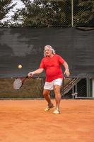 anziano tennis giocatore vestito nel abbigliamento sportivo nel azione su un' argilla tennis Tribunale foto