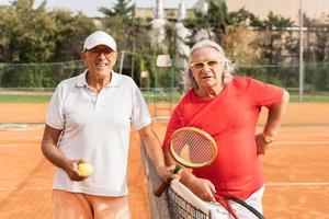 ritratto di Due anziano tennis Giocatori vestito nel abbigliamento sportivo tremante mani su un' argilla tennis Tribunale foto