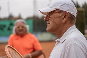 ritratto di Due anziano tennis Giocatori vestito nel abbigliamento sportivo rilassante a il fine di il gioco su un' argilla tennis Tribunale foto