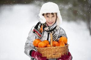 bello poco ragazzo nel inverno Abiti Tenere un' cestino di arance. foto