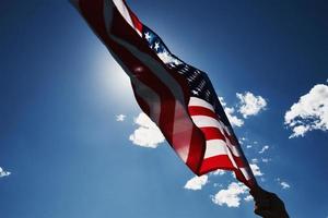 agitando Stati Uniti d'America bandiera nel mano contro blu cielo foto