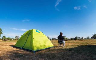 le turiste asiatiche sono sedute felici libere con la tenda verde per il viaggiatore che si siede su un ampio campo, affacciandosi sull'ora serale dell'area privata thailandese per una vacanza in campeggio durante una lunga vacanza per viaggiare. foto