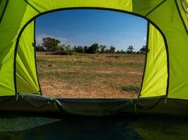 viaggiatore verde tenda campeggio all'aperto viaggio. Visualizza a partire dal il tenda dentro su il blu cielo sole nel il estate paesaggio. durante il sera di il giorno adatto per addormentato e riposo il corpo foto