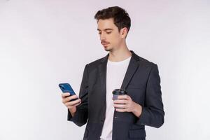 ritratto di un' contento uomo d'affari utilizzando smartphone e Tenere caldo caffè al di sopra di bianca foto