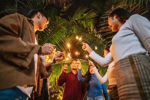 ritratto di contento asiatico gruppo di amici avendo divertimento con sparklers all'aperto - giovane persone avendo divertimento con fuochi d'artificio a notte tempo - le persone, cibo, bevanda stile di vita, nuovo anno celebrazione concetto. foto