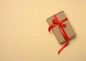 rettangolare Marrone cartone scatola legato con un' seta rosso nastro su un' beige sfondo, superiore Visualizza foto