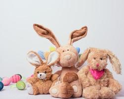tre felpa giocattoli coniglietto sedersi su un' bianca sfondo, dietro a decorativo Pasqua uova foto