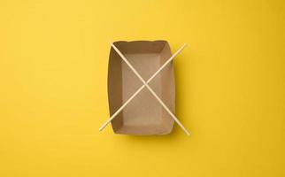 vuoto Marrone carta piatto e di legno bastoncini su un' giallo sfondo, superiore Visualizza foto