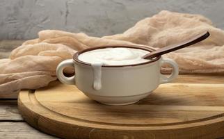 acida crema nel un' Marrone ceramica ciotola con un' di legno cucchiaio su un' di legno tavola sfondo foto