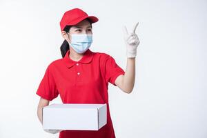 Immagine di un' consapevole giovane consegna uomo nel rosso berretto vuoto maglietta uniforme viso maschera guanti in piedi con vuoto bianca cartone scatola isolato su leggero grigio sfondo studio foto