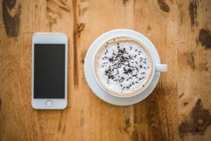 una tazza di caffè e smartphone sul tavolo di legno nella caffetteria foto