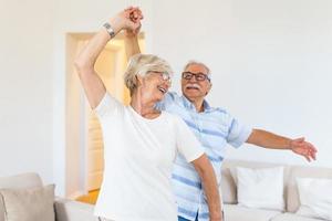 spensierato contento attivo vecchio anziano coppia danza salto ridendo nel vivente camera, allegro pensionato Sambuco marito Tenere mano di maturo mezzo anziano moglie godere divertimento tempo libero la pensione stile di vita a casa foto