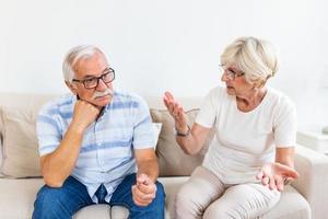 anziano coppia avendo discussione su il divano a casa nel il vivente camera. donna e uomo emozioni Esprimere a gesti con mani. anziano coppia discutere foto