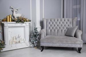 divano grigio velluto con piccolo albero di natale, falso camino e decorazioni natalizie foto