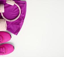 un' paio di tessile viola gli sport scarpe da ginnastica, senza fili cuffia, un' asciugamano e un' bottiglia di acqua su un' bianca sfondo. abbigliamento sportivo foto