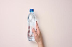 femmina mano detiene un' plastica trasparente bottiglia su un' beige sfondo foto