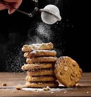 un' pila di al forno il giro biscotti cosparso con in polvere zucchero su un' di legno tavolo, nero sfondo foto