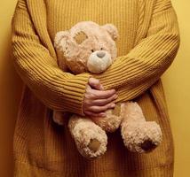 donna nel arancia a maglia maglione abbracci carino Marrone orsacchiotto orso. il concetto di solitudine e tristezza, depressione foto