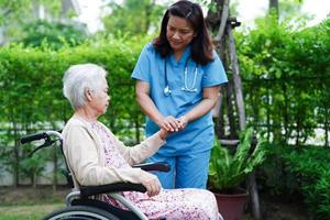 il medico aiuta il paziente asiatico della disabilità della donna anziana che si siede sulla sedia a rotelle nel parco, concetto medico. foto