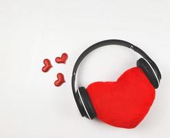 piatto posare di rosso cuore cuscino coperto con cuffie isolato su bianca sfondo decorato con rosso luccichio cuore.. amore canzoni o Podcast concetto. foto