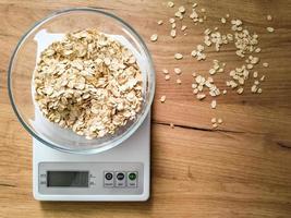 fiocchi d'avena pesatura nel bicchiere ciotola su il cucina bilancia su di legno tavolo. foto