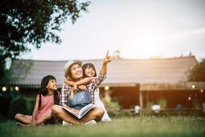 madre che racconta una storia alle sue due figlie piccole nel giardino di casa foto